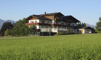 A large, elegant house surrounded by a green meadow. In the background, gentle hills and trees are visible.