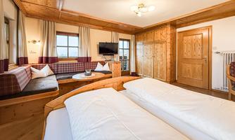 A cozy room with wooden paneling and two single beds. There is a seating area and a television.