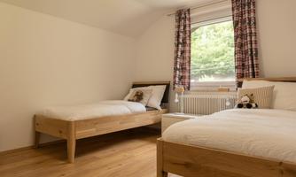 A cozy bedroom with two wooden beds. The window lets in plenty of light and there are a few decorative pillows and plush toys.