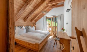 A cozy bedroom with a wooden ceiling and two beds. Large windows offer a view of nature.