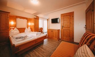 A cozy bedroom with wooden furniture and a large bed. The room is bright and friendly with a television on the wall.