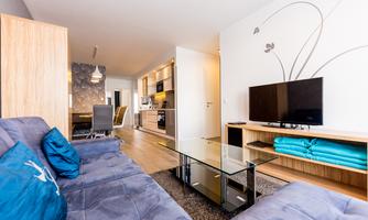 A modern living room with a blue sofa and a glass coffee table. The open kitchen and the television create a cozy atmosphere.