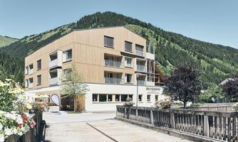 A modern building in a mountainous landscape. Surrounded by trees and flowers, it radiates an inviting atmosphere.