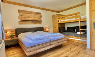 A cozy bedroom with a double bed and a bunk bed. The room features wooden furniture and warm lighting.