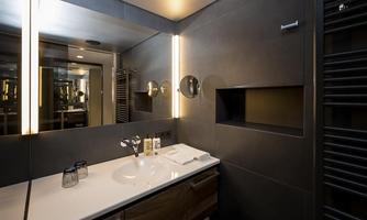 A modern bathroom with an elegant sink unit and stylish lighting. The walls are in dark colors, complemented by wooden accents.