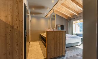 A modern bedroom with wood paneling and a large window. The ceiling is made of wood and the floor has an appealing pattern.