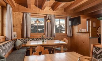 A cozy restaurant with wooden furniture and large windows that offer a view of the mountains. The space is brightly lit and invitingly designed.