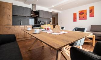 A modern apartment with a wooden tray and a beautiful dining table. The walls are decorated with red pictures, and the kitchen is well-equipped.