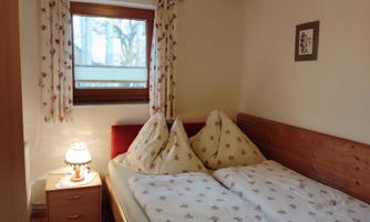 A cozy bedroom with a double bed and floral bedding. A window with curtains and a bedside lamp create an inviting atmosphere.