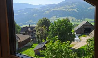 A picturesque view of green hills and mountains through a window. In the foreground, there are trees and typical country houses.