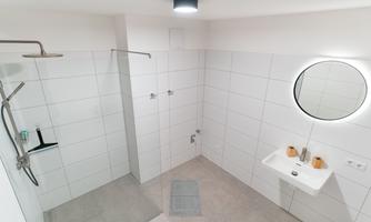 A modern bathroom with a glass shower and a round mirror. The walls are tiled in light colors.
