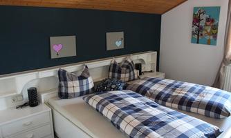 A cozy bedroom with a double bed and checkered bed covers. The walls are painted in soft colors and there are decorative pictures.