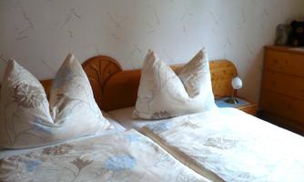 A cozy bedroom with two beds and decorative pillows. The wall is painted light, and a night lamp is on the nightstand.