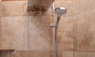 A modern shower system with a large, flat overhead shower and a handheld shower. The walls are clad with light tiles.