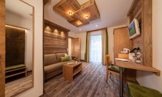 A modern room with wooden paneling and pleasant light. There is a sofa, a table, and a view of a balcony with curtains.