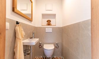 A modern and stylish guest toilet with a bright tiled floor and a small sink. A towel hangs on the wall, and a decorative piece is placed on a shelf.