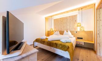 A modern bedroom with wooden paneling and a large bed. A TV stands on a wooden cabinet, and soft lighting creates a cozy atmosphere.