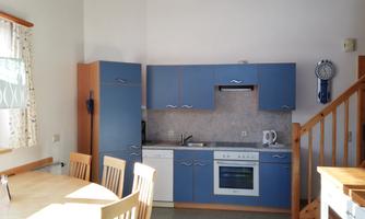 A modern kitchen with blue cabinets and a dining table. Bright walls and plenty of daylight create an inviting atmosphere.