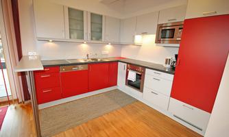 A modern kitchen with red and white furniture. There is a table and a kitchenette with a stove and microwave.