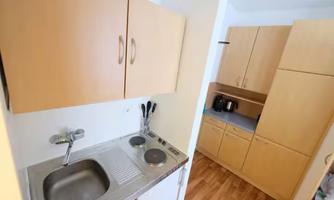 A small kitchen with wooden furniture and a stainless steel sink. In the background, there is a refrigerator and additional kitchen cabinets.