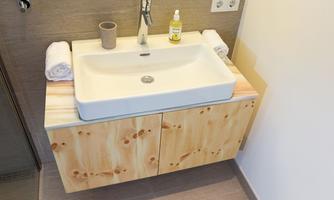 A modern bathroom with a white sink on a wooden shelf. It includes fresh towels and toiletries on the surface.