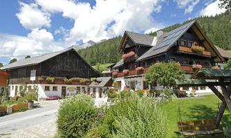 A picturesque farmhouse with colorful flowers and a green garden. The surroundings feature tall trees and a clear sky.