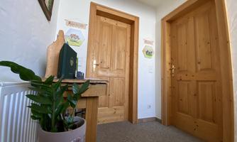 A bright hallway with two wooden doors and a small table. On the table sits a green plant and two pictures hang on the wall.