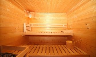 A cozy sauna with wooden walls and wooden benches. On one of the benches, there is a bucket and a ladle.