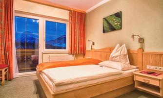 A cozy bedroom with a double bed and wooden furniture. Through the window, you can see the mountains and the evening sky.