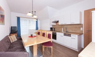 A modern kitchen with a dining area and a cozy sofa. Bright walls and wooden details create an inviting atmosphere.