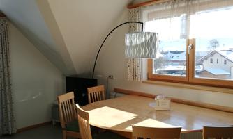 A cozy dining area with a round table and chairs. A large window lets daylight in and offers a view outside.