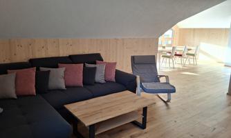 A cozy living room with a large sofa and a wooden table. Bright walls and a spacious, inviting atmosphere.