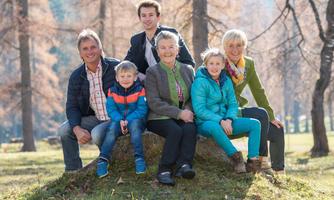 A cheerful family is sitting on a log in the park. In the background, autumn trees with yellow and brown leaves can be seen.