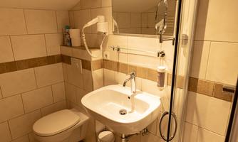 A modern bathroom with tiles and a sink. The shower is separated by a glass door.