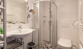 A modern bathroom with a shower, a sink, and a toilet. The walls are brightly tiled, and there is a mirror above the sink.