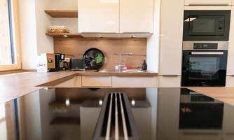 A modern kitchen with wood and white elements. The equipment includes a cooktop, a sink, and various appliances.