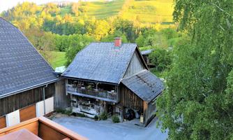 A charming country house with a balcony, surrounded by green meadows. In the background, gentle hills can be seen.