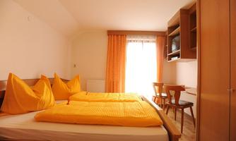 A bright room with a double bed and yellow pillows. There is a desk, a chair, and a lot of daylight through the window.
