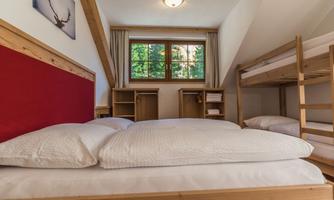 A cozy bedroom with a double bed and bunk bed. There are wooden cabinets and a window with a view to the outside.
