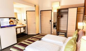A modern hotel room with two beds, a large television, and a closet. The room is bright and friendly with a cozy decor.