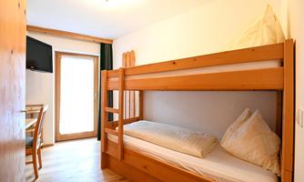 A simple room with a wooden loft bed. There is a table and a television, as well as a balcony with sunlight.