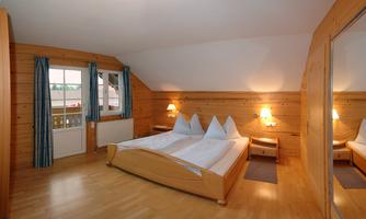 A cozy room with wooden paneling and a double bed. Large windows provide plenty of daylight.