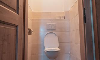 A modern bathroom with a white toilet and wooden floor. The walls are light tiled and the light is pleasant.