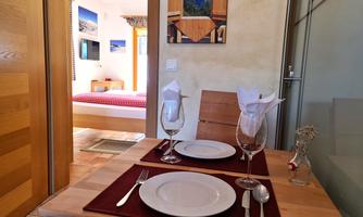 A cozy table set with plates and glasses. In the background, a bedroom with a red bed can be seen.