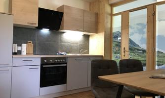 A modern kitchen with wood and gray accents. The dining area is bright and inviting, with a view of nature through the windows.