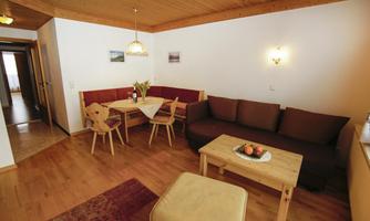 A cozy apartment with a wooden ceiling and warm tones. The room contains a seating area, a dining table, and some decorations.