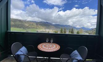 A quiet balcony with two chairs and a round table. In the background, the mountains and the blue-and-white sky are visible.
