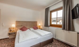 A cozy bedroom with a double bed, nightstands, and two lamps. A window lets in daylight and offers a view outside.