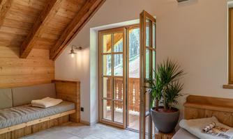 A cozy room with wooden walls and sloped ceilings. Large windows provide a view outside, and a green plant adds to a relaxed atmosphere.