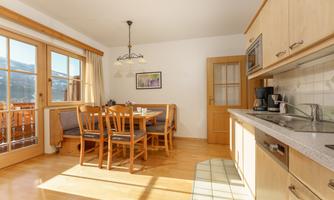 A bright kitchen with a dining area and a large window. The table is surrounded by wooden chairs and the walls are painted light.